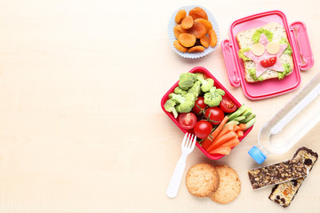 School lunch box with vegetables and bottle of water on wooden table