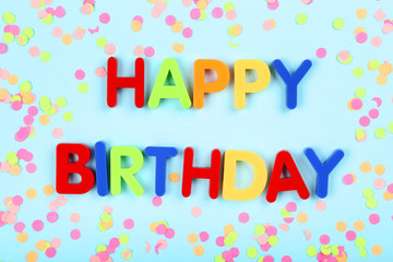 Text Happy Birthday by plastic letters with confetti on blue background