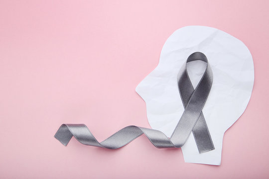 Grey ribbon and head shape from paper on pink background. Brain cancer concept