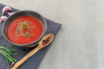 Cold tomato gazpacho soup in a deep plate on a stone background. Traditional Spanish cuisine. The concept of Spanish cold soup of ripe tomatoes. Copy space, close-up.