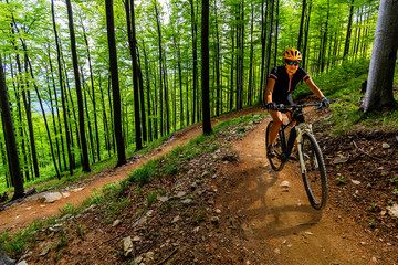 Fototapeta na wymiar Mountain biking woman riding on bike in summer mountains forest landscape. Woman cycling MTB flow trail track. Outdoor sport activity.