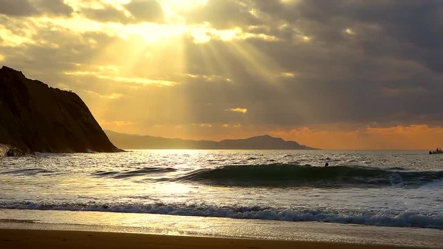 Golden sunset with sun's rays over the ocean. Boat and boogie boarders.Itzurun beach, flysch of Zumaia on the coast of Gipuzkoa, Spain. Outdoor fitness lifestyle.
