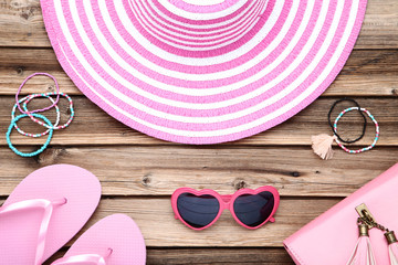 Beach hat with sunglasses, flip flop and bracelets on brown wooden table