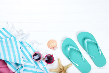 Pair of flip flops with seashells, towel and sunglasses on white wooden table