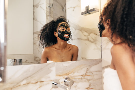 Smiling woman with black cosmetic mask on face in bathroom