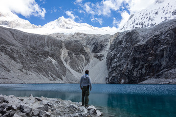 Back of a young backpacker standing in front of the turquoise glacier lake in Huascaran National Park, Laguna 69, Peru