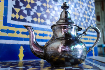 Silver metal tea kettle with mosaics background standing in a palace in Fez, Morocco