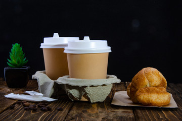 Paper cups of coffee, sugar in bags, donuts. Croissant. Wooden table. Black background.