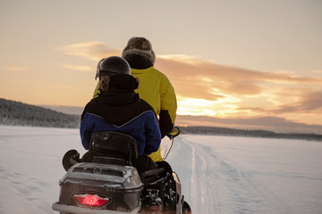 2 people riding on a snowmobile through the wilds of Lapland