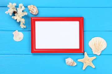 Wooden blank frame with seashells on blue table