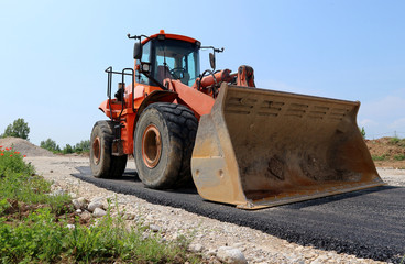 Obraz na płótnie Canvas Large orange bulldozer on a half paved road at the construction site
