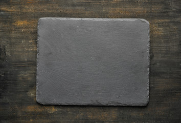 Black stone cutting board on old wooden table, from above