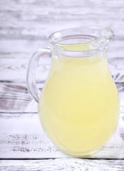Milk whey in a glass jug against the white wooden background