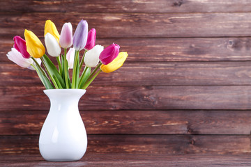 Bouquet of tulip flowers in vase on brown wooden background