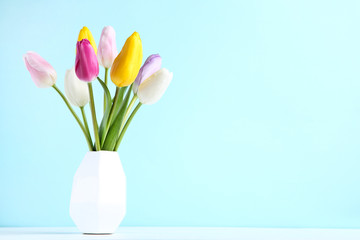 Bouquet of tulip flowers in vase on blue background