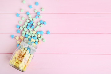 Colorful paper stars in glass jar on pink background