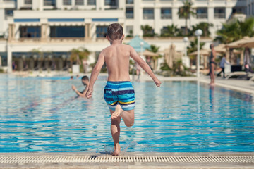 Boy running to jump into swimming pool at resort.