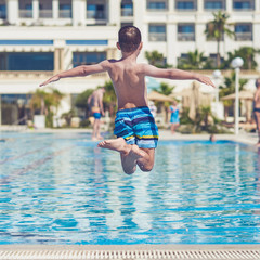 Boy having fun making fantastic jump into swimming pool. His arms are wide open.