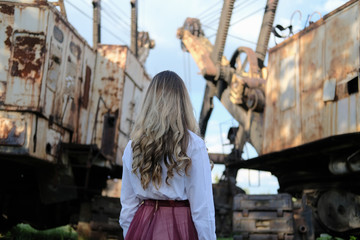 Fototapeta na wymiar beautiful young girl on the background of industrial landscape and old construction equipment. portrait in grunge style. the concept of loneliness and the world of technology.