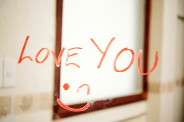 Confession of love and smiley face written with red lipstick on the mirror in bathroom