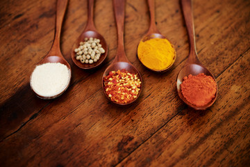 Composition with different spices on wooden spoons on wooden background