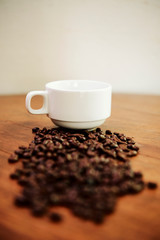 Close-up of black coffee beans lying on wooden table with cup in the background