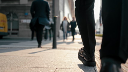 Close Up Unrecognizable Business Man Legs in Suit and Shoes Walking Outdoors in the Center of Big City with Blurred Pedestrians in Busy Street in Spring Sunny Day