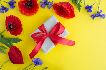 Gift box with red ribbon,red poppies and cornflowers on the yellow  background.Top view.Copy space.