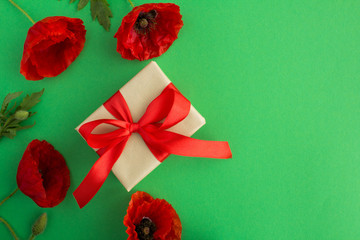 Gift box with red ribbon  and red poppies on the green background.Top view.Copy space.