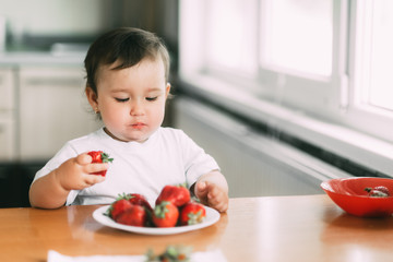Little girl child in white t-shirt eating strawberries all smeared and dirty