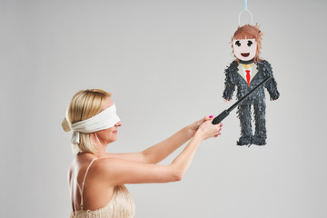 Woman hitting male pinata over grey background