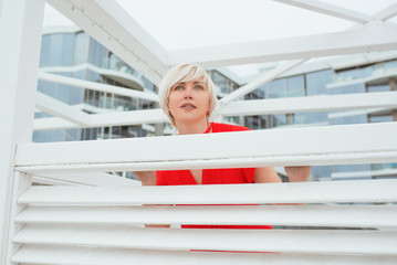 portrait of pretty cool beautiful short hair blonde woman in red coral dress near wooden white arbor for the beach