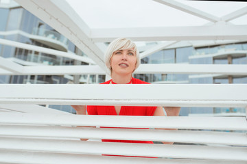 portrait of pretty cool beautiful short hair blonde woman in red coral dress near wooden white arbor for the beach