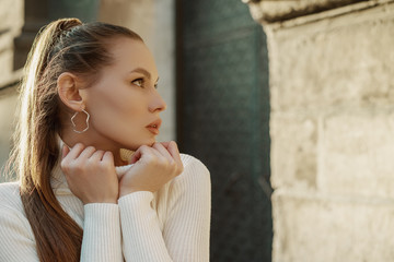 Outdoor close up portrait of young beautiful fashionable woman with long hair wearing trendy hoop...