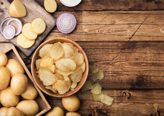 Obraz na płótnie Canvas Fresh organic homemade potato crisps chips in wooden bowl with sour cream and red onions and spices on wooden table background. Top view.Fresh yellow potatoes with ketchup