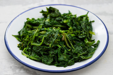boiled greens with garlic on white plate on ceramic background