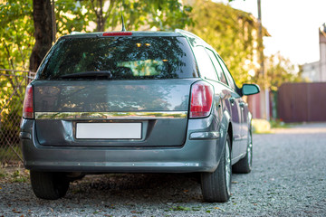 New shiny gray car parked on gravel suburbs road on blurred sunny summer background.