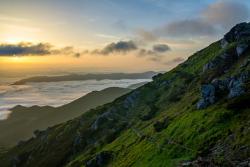 Fantastic view of mountain valley covered with low white puffy like snow clouds stretching to foggy horizon under bright morning sky with light orange glow at sunrise. Beauty of nature concept.