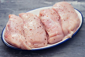 raw chicken breasts on white dish on ceramic background