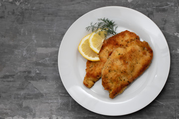 fried chicken with lemon on white plate on ceramic background
