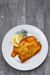 fried chicken with lemon on white plate on ceramic background