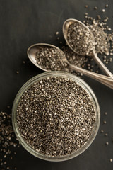 Chia seeds in glass bowl isolated on wooden background, selective focus. Dark background.