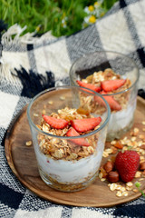 Yogurt with granola and strawberries in a glass on natural background Summer picnic