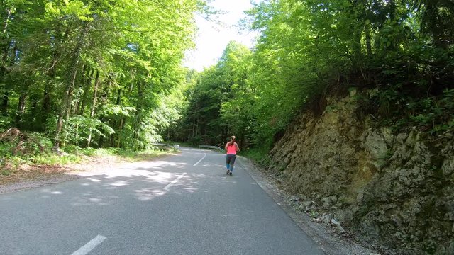 Forward tracking shot of an overweight woman on her daily run up a forest road in sunshine