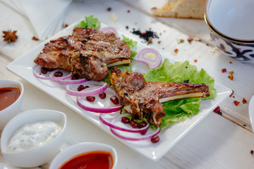 Barbecue ribs on white plate, meat dish served with onion and herbs.