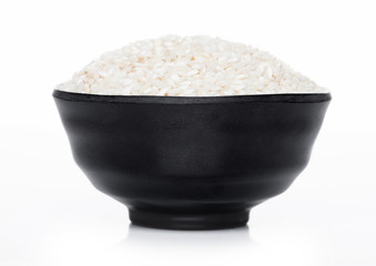 Black bowl of raw organic arborio risotto rice on white background. Healthy food.