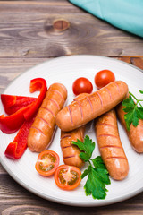 Grilled sausages, fresh tomatoes, peppers and parsley on a plate on a wooden table