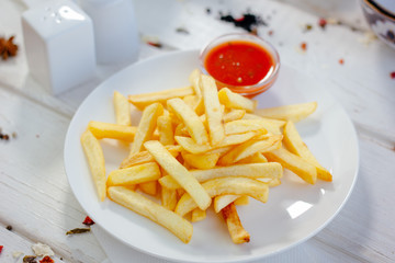 French fries with red tomato sauce on the white plate.
