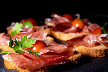 jamón serrano sobre pan tostado con tomate cherry y perejil, en clave oscura y presentado en plato...
