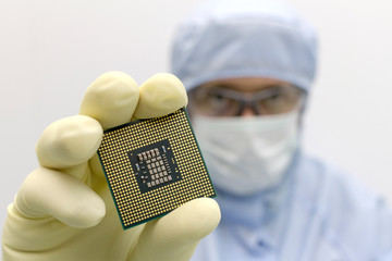 An engineer working in a clear room wearing a special uniform and protective glasses holds processor cpu in hand in glove